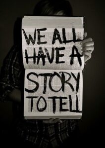 A book with bold texts written in black that says, "WE ALL HAVE A STORY TO TELL"